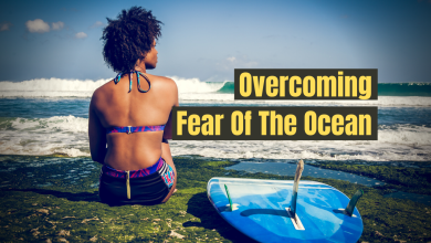 A woman sitting on the beach next to a surfboard with the words "Overcoming fear of the ocean"