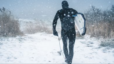man carrying surfboard walking on snow