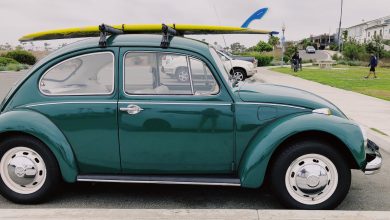 empty green Volkswagen Beetle carrying yellow surfboard on parking lot during daytime